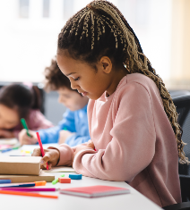 Young girl leaning over her desk as she completes a project with paper and pen
