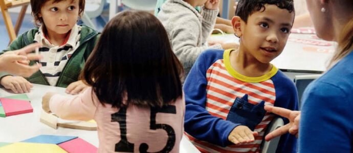Young boy leaning back at a school table to talk to a teacher