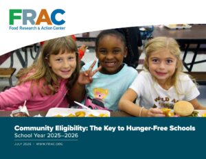Three young girls smiling at the camera as they eat lunch in a school
