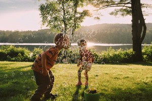 Two children in a front yard blowing bubbles in the sunshine