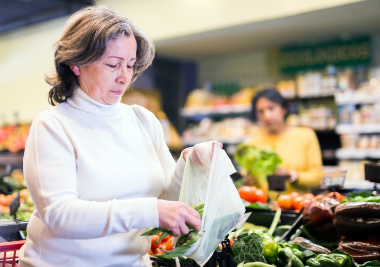 Older woman in white shirt picking out produce at a grocery store