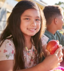 Young female student eating an apple outside on a schoolyard