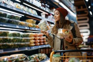 Younger woman in beanie hat looking at items in the dairy section of a grocery store